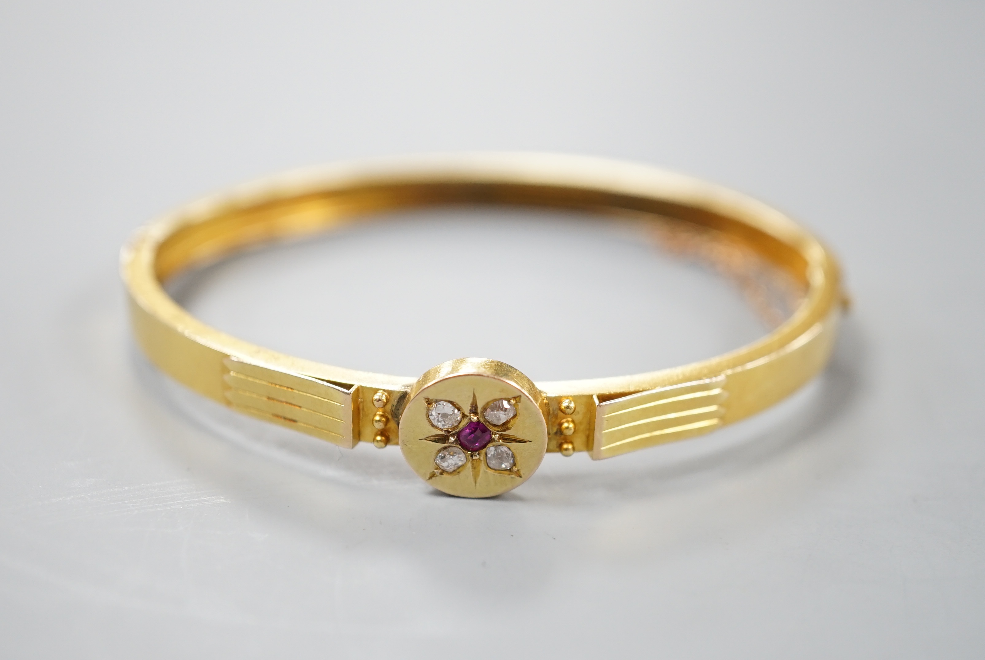 An early 20th century yellow metal, ruby and diamond cluster set hinged bangle, gross 8.9 grams.